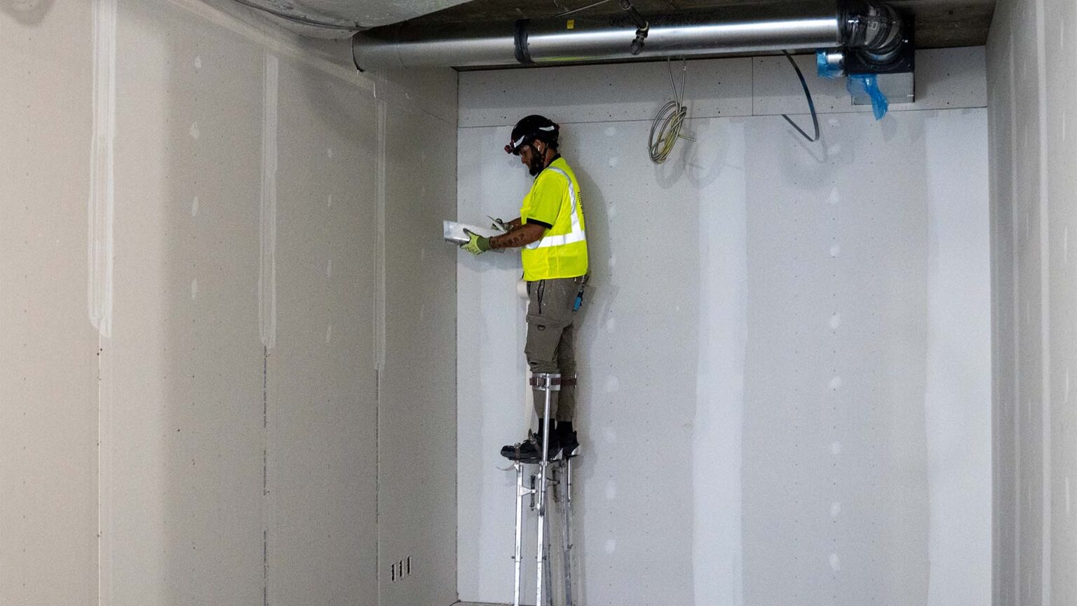 Drywall finisher mixing compound as he stands inside a office room under construction